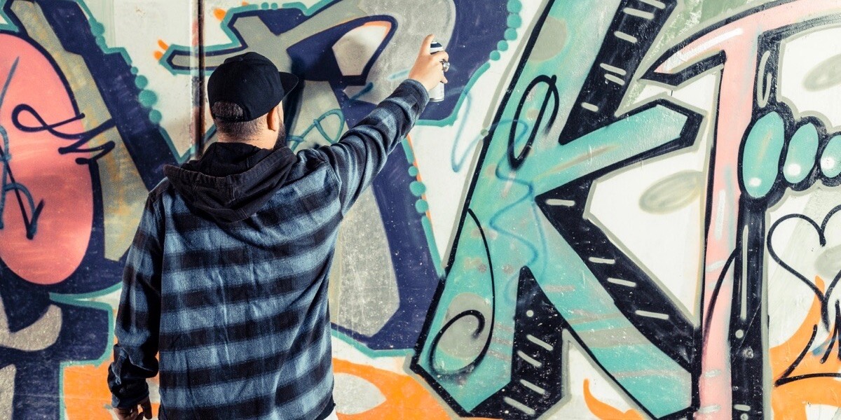 A man seen from behind creating graffiti on a wall